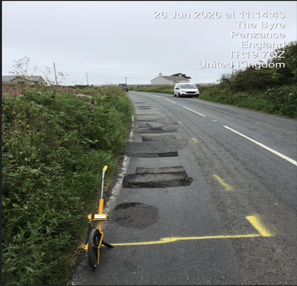 Patched road edge near Penzance with yellow repair markings and a measuring wheel