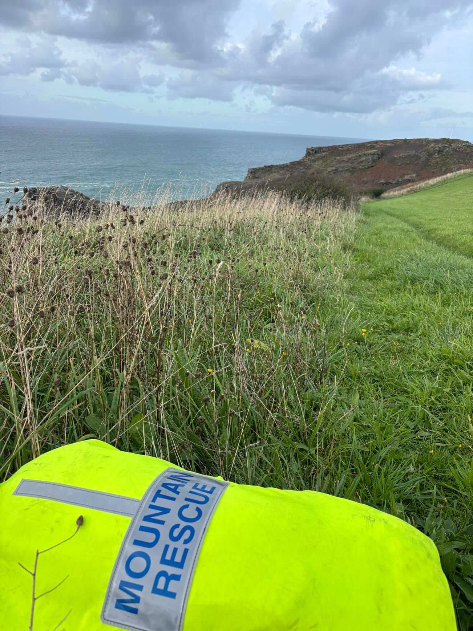 A hi-vis Mountain Rescue jacket in the foreground of a clifftop field overlooking the sea