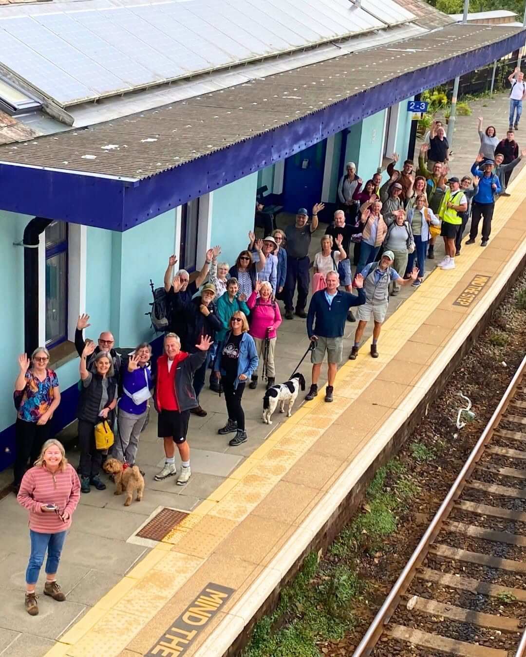Walkers waving from a railway station platform
