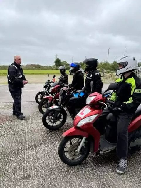 Young riders on mopeds and motorcycles listening to a Gear Up instructor