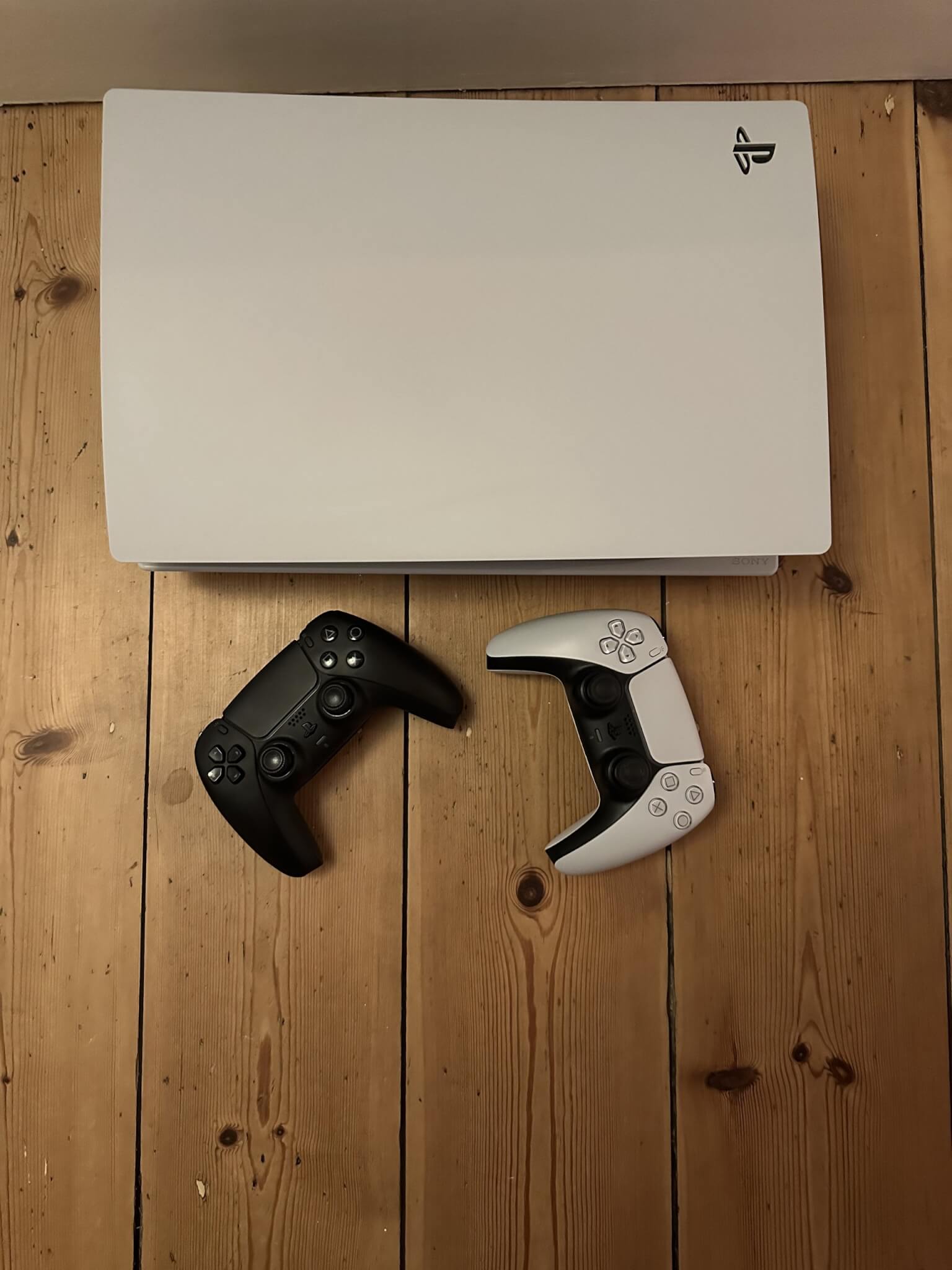 A games console and two controllers on a wooden floor