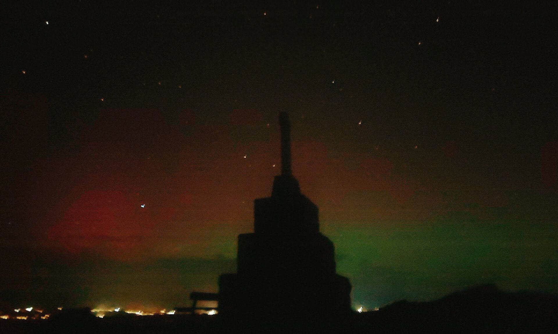 Stone memorial silhouetted against a starry night sky with red and green aurora