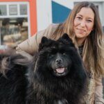 Woman crouching with a large black fluffy dog and a small white dog outside a building painted with a Union flag