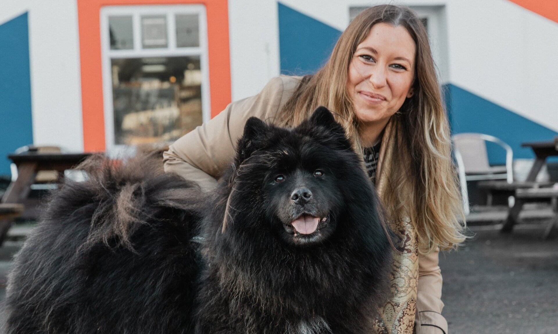 Woman crouching with a large black fluffy dog and a small white dog outside a building painted with a Union flag