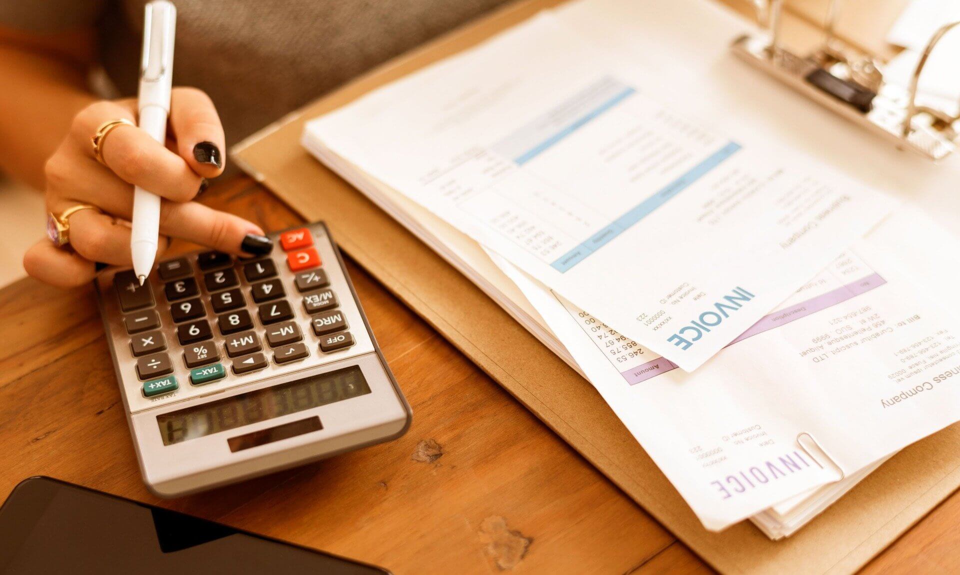 A hand using a calculator beside a folder of invoices