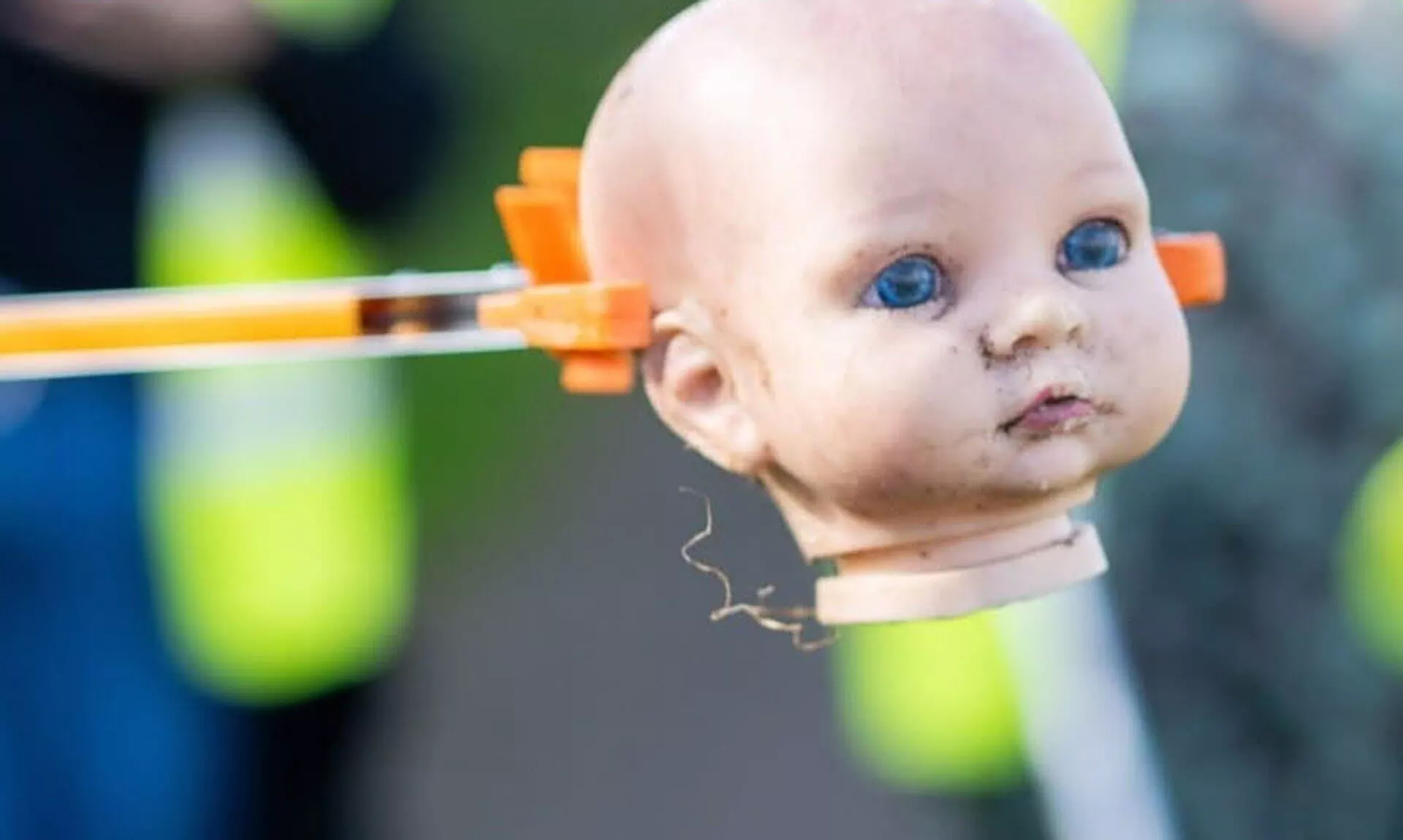 A discarded doll's head held in a litter picker during a clean-up