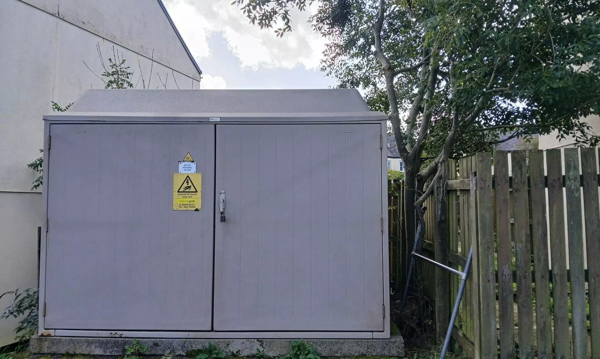 Electricity substation with a fibreglass roof beside a house and fence