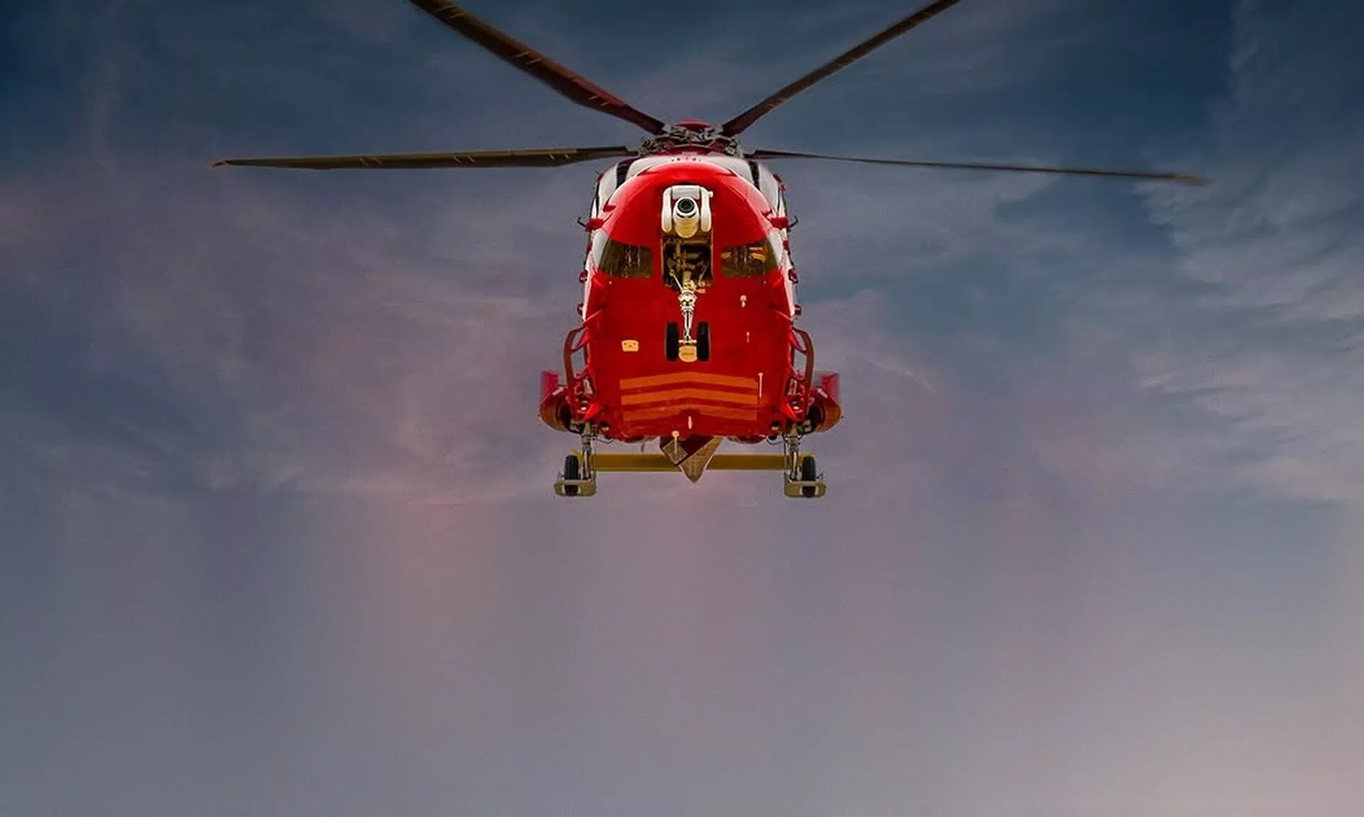 Red Cornwall Air Ambulance helicopter hovering against an evening sky