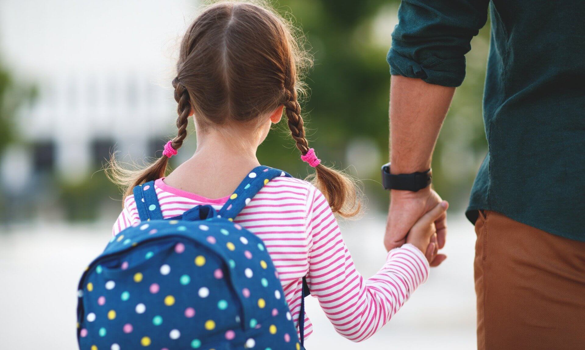 A young girl with a school backpack holding a parent's hand