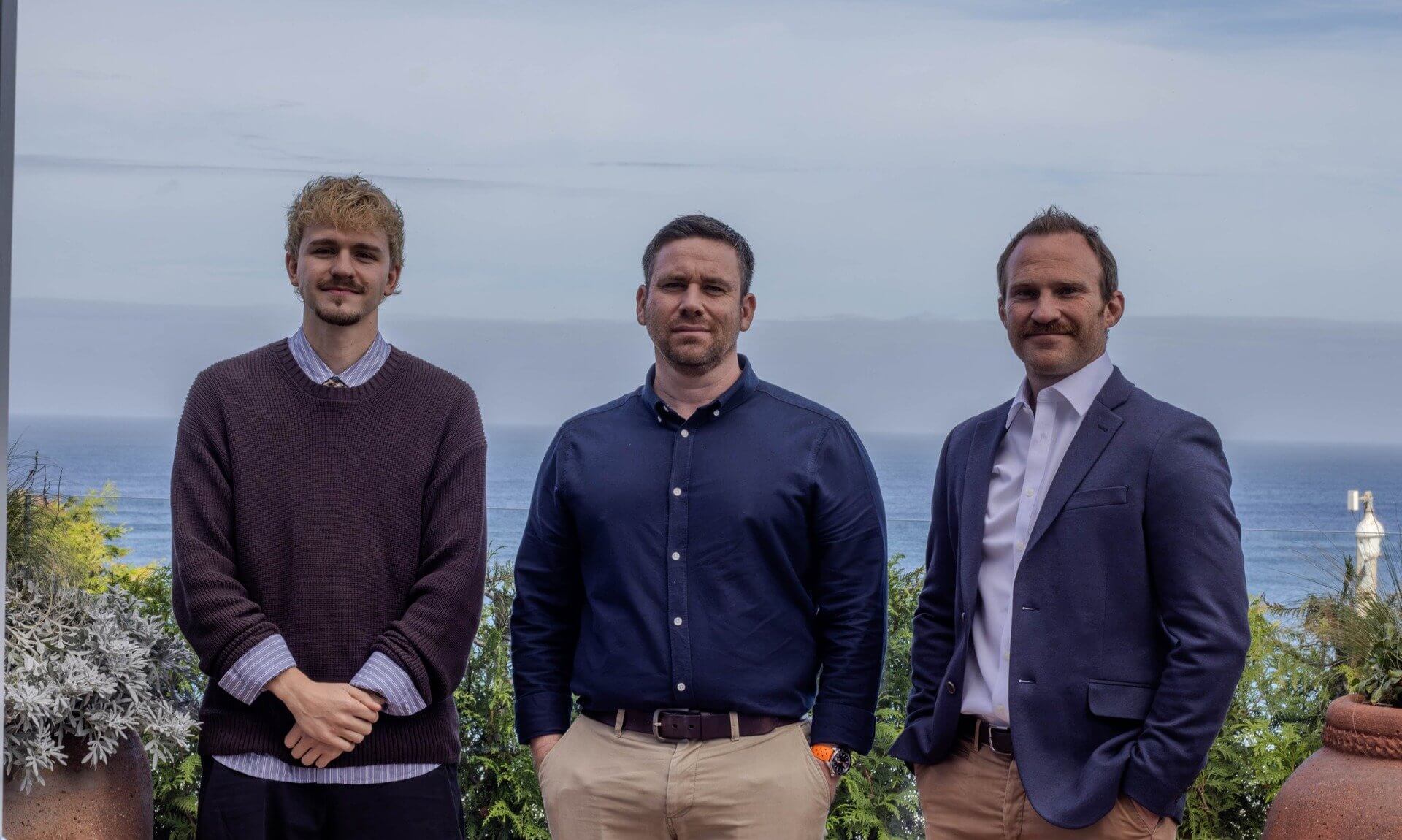 Three men standing on a terrace overlooking the sea in Cornwall