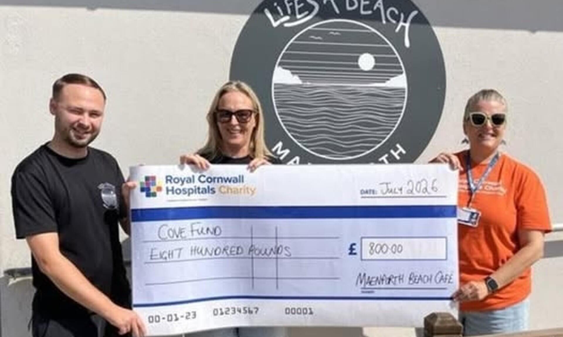 Cheque for £800 presented to Royal Cornwall Hospitals Charity outside Life's A Beach Cafe, Mawgan Porth