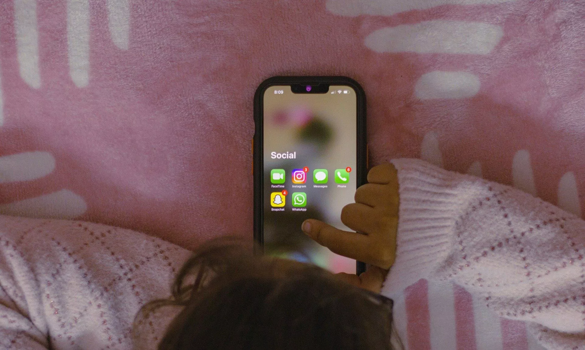 A child lying on a pink blanket looking at social media apps on a phone