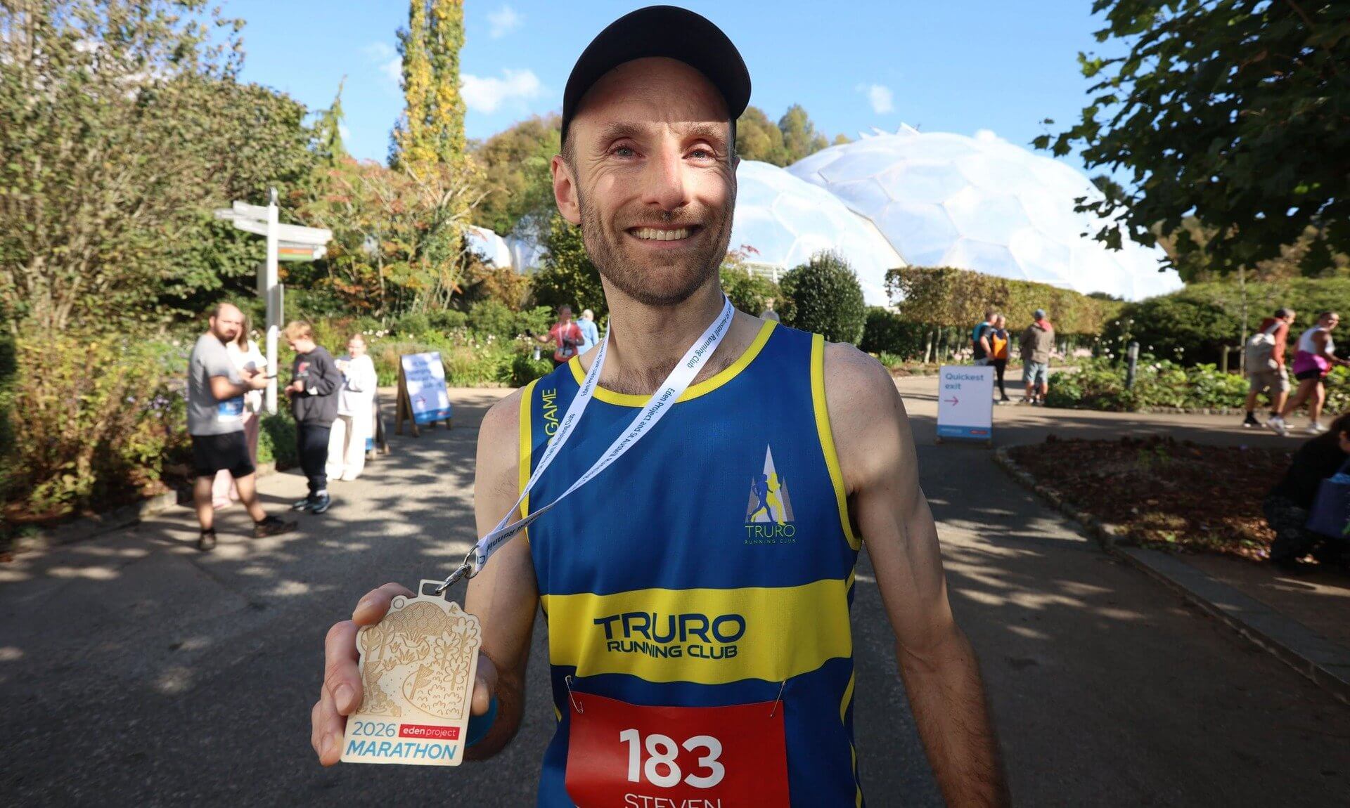 Steven Reynolds holding his medal in front of the Eden Project Biomes