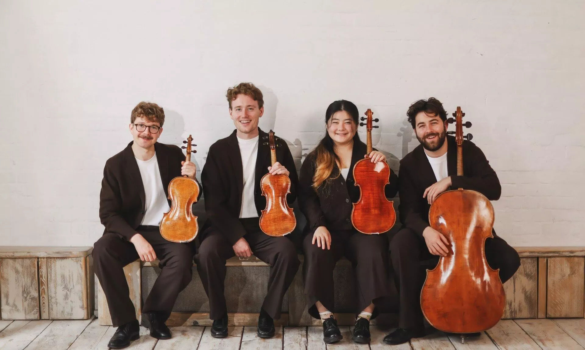 The Elmore Quartet sitting on a bench holding their violins, viola and cello