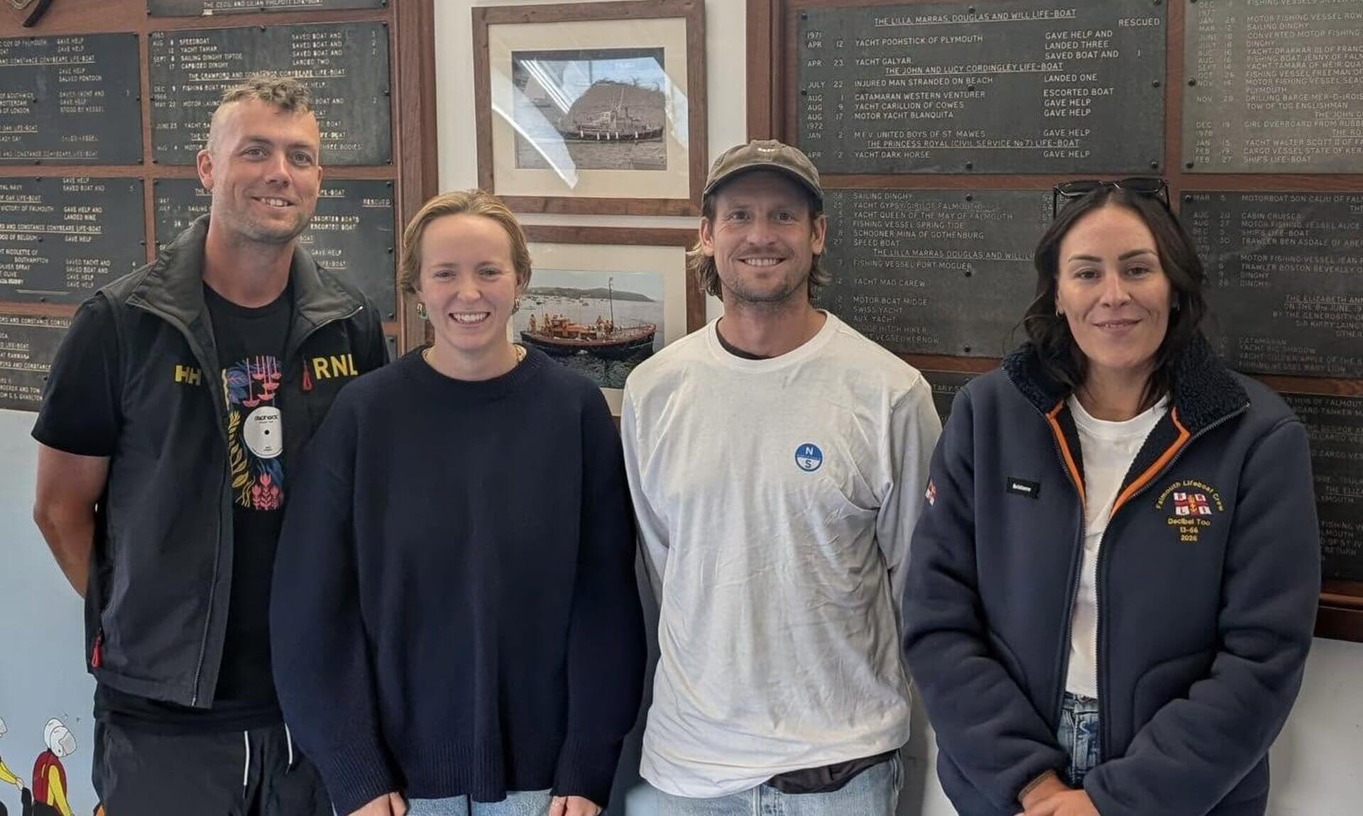 Four Falmouth Lifeboat volunteers in front of the station's service record boards