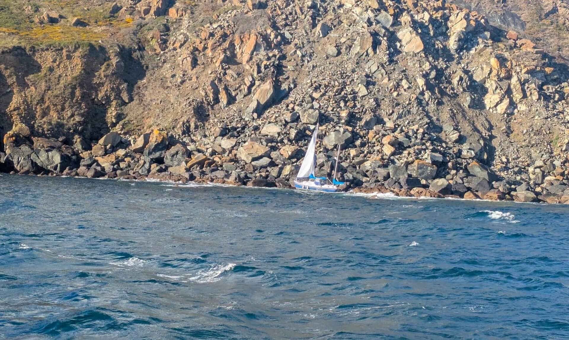 Damaged yacht pinned against rocks below cliffs near Black Head on The Lizard