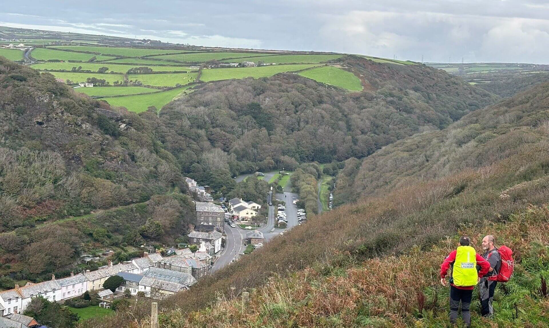 Two mountain rescue volunteers on a hillside looking down over Boscastle village and valley