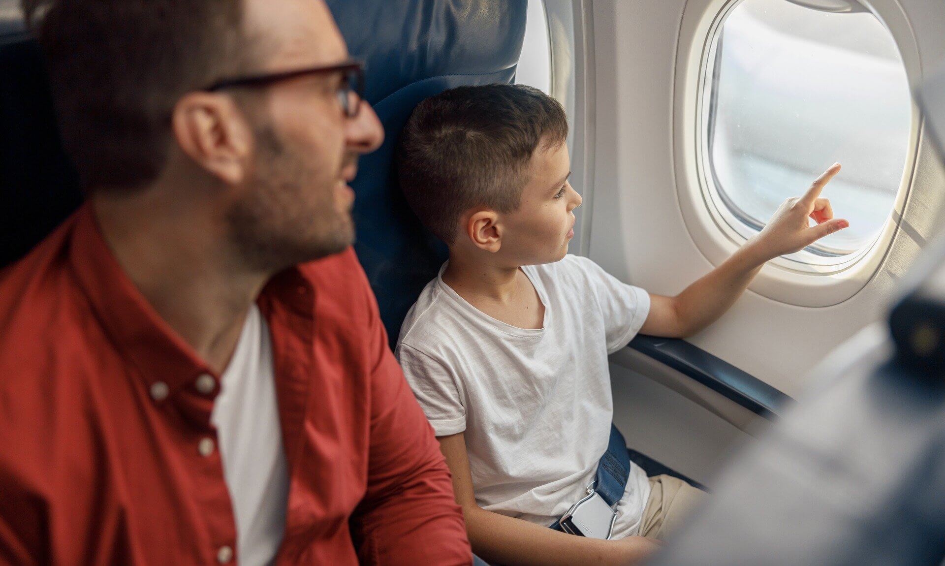 A father and his young son sitting together on a plane, the boy pointing out of the window