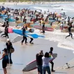Hundreds of surfers carrying boards into the sea at an Earthwave event