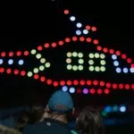 Drones forming a red helicopter shape above a crowd at night