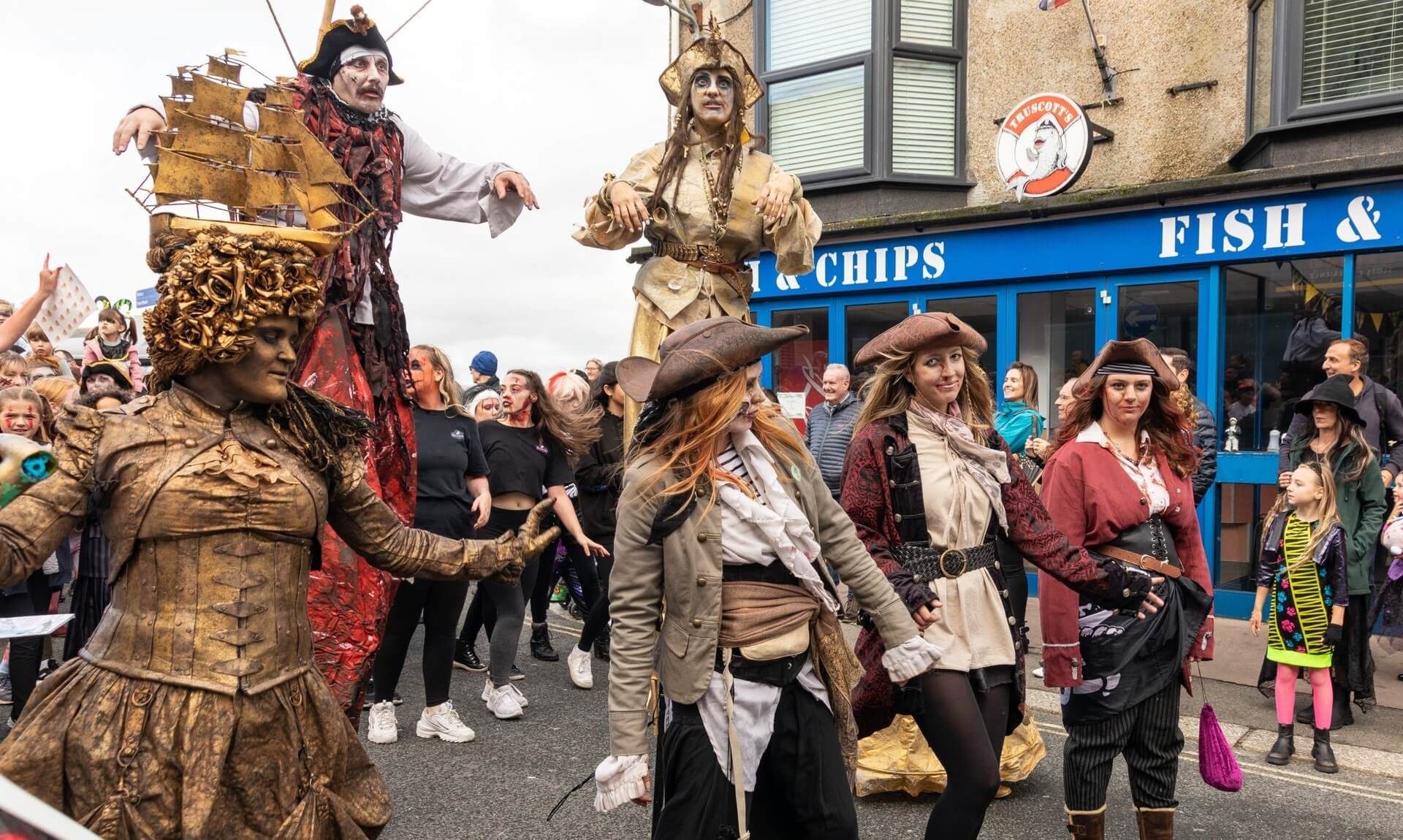 Stilt walkers and costumed pirates leading the Newquay Zombie Crawl past a fish and chip shop