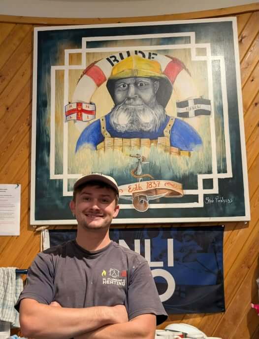 Bude RNLI crew member Noah Lakeland in front of a lifeboat painting at the station