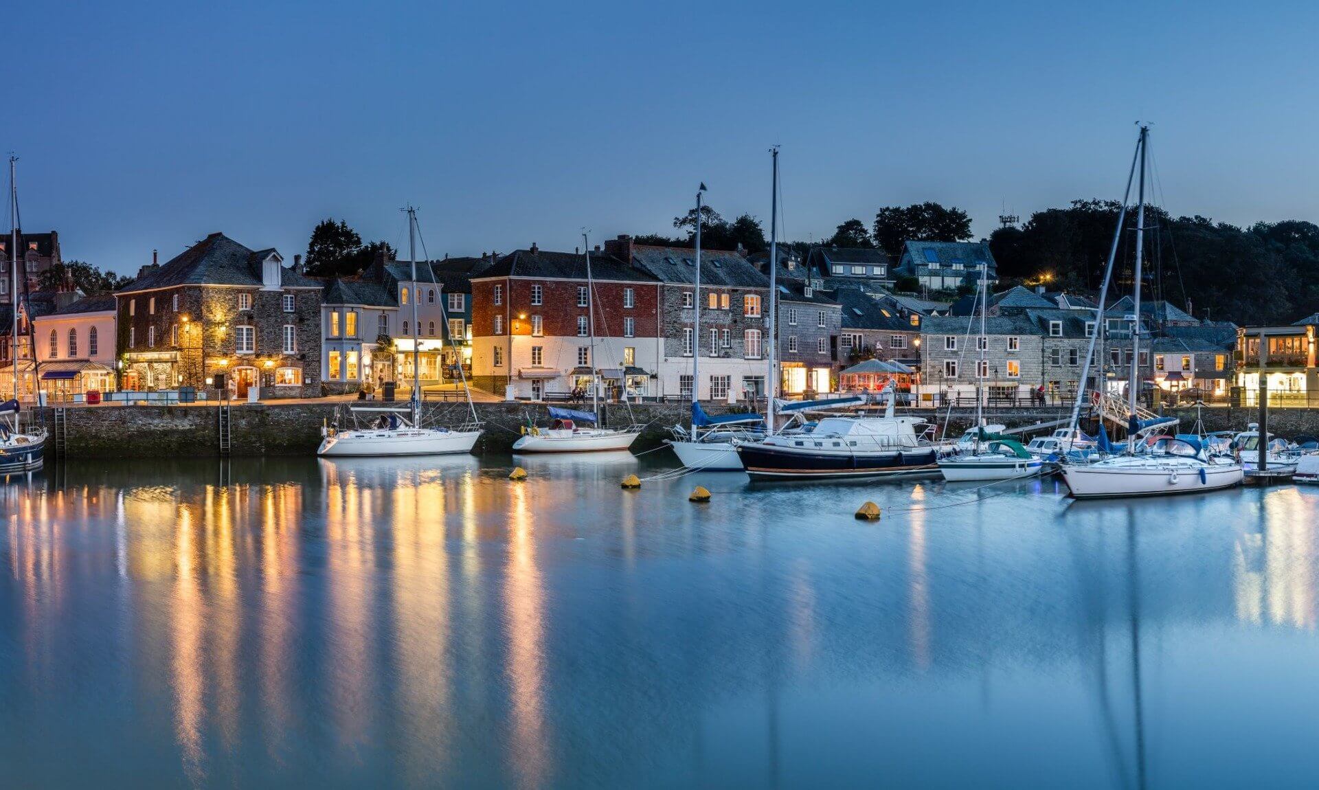 Padstow harbour at dusk with boats moored and lights reflecting on the water