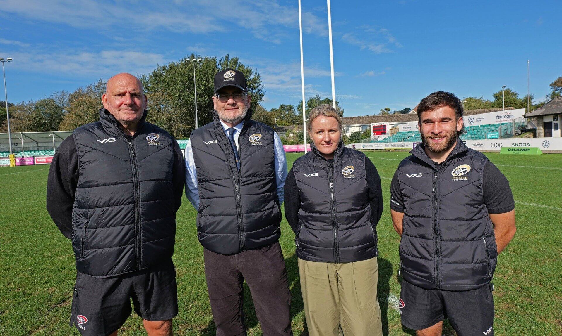 Four people in Pirates Foundation gilets standing on a rugby pitch in front of the posts