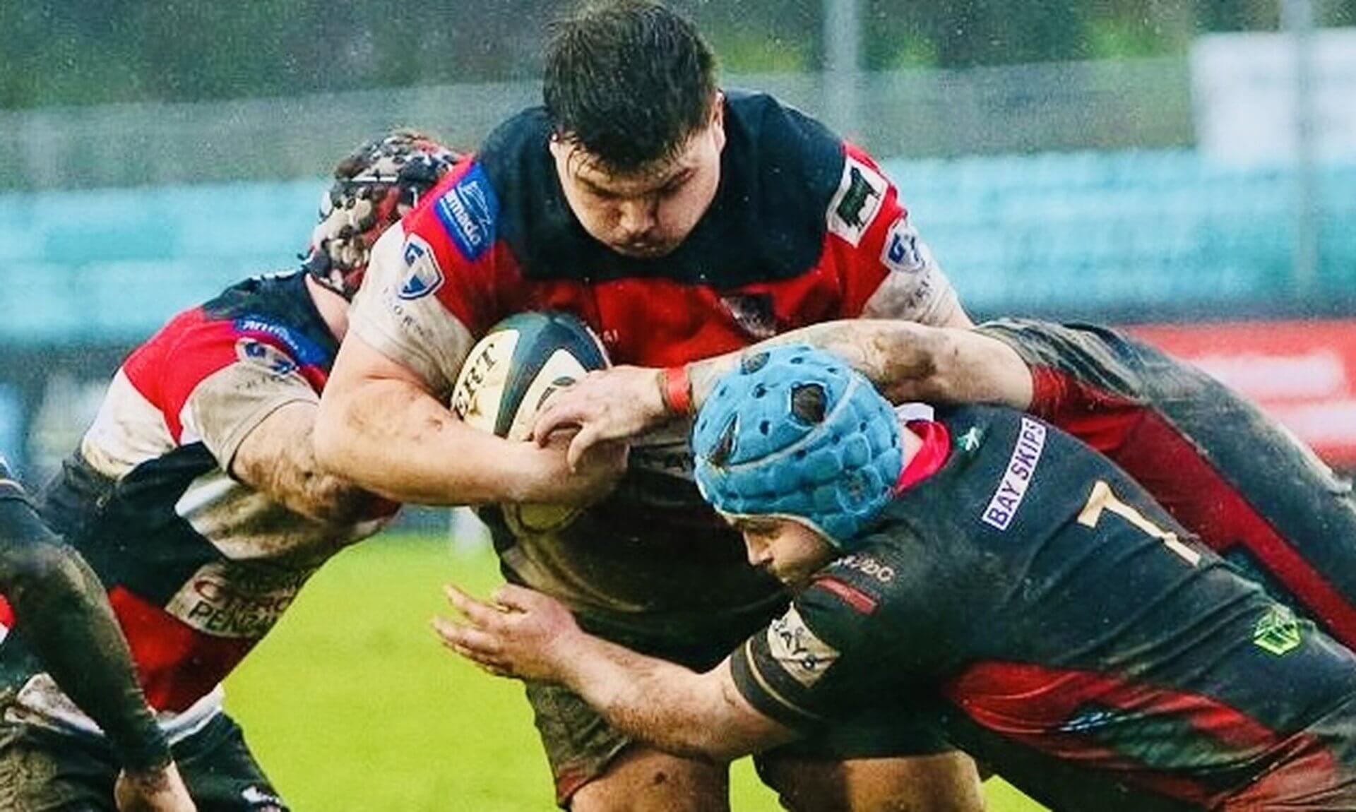 Penzance & Newlyn prop carries the ball into Okehampton defenders on a muddy pitch