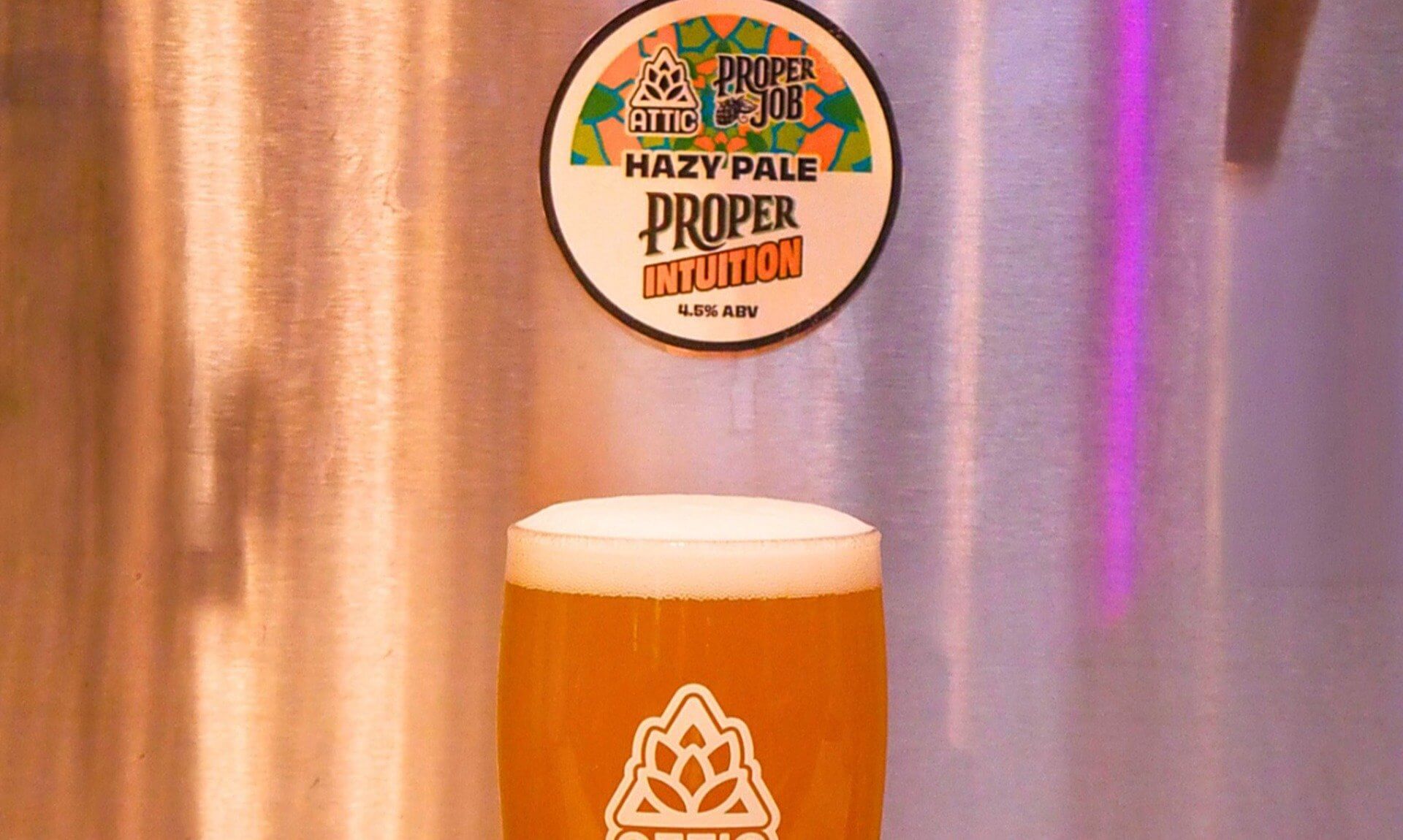 A pint of Proper Intuition hazy pale ale in an Attic glass below the tap