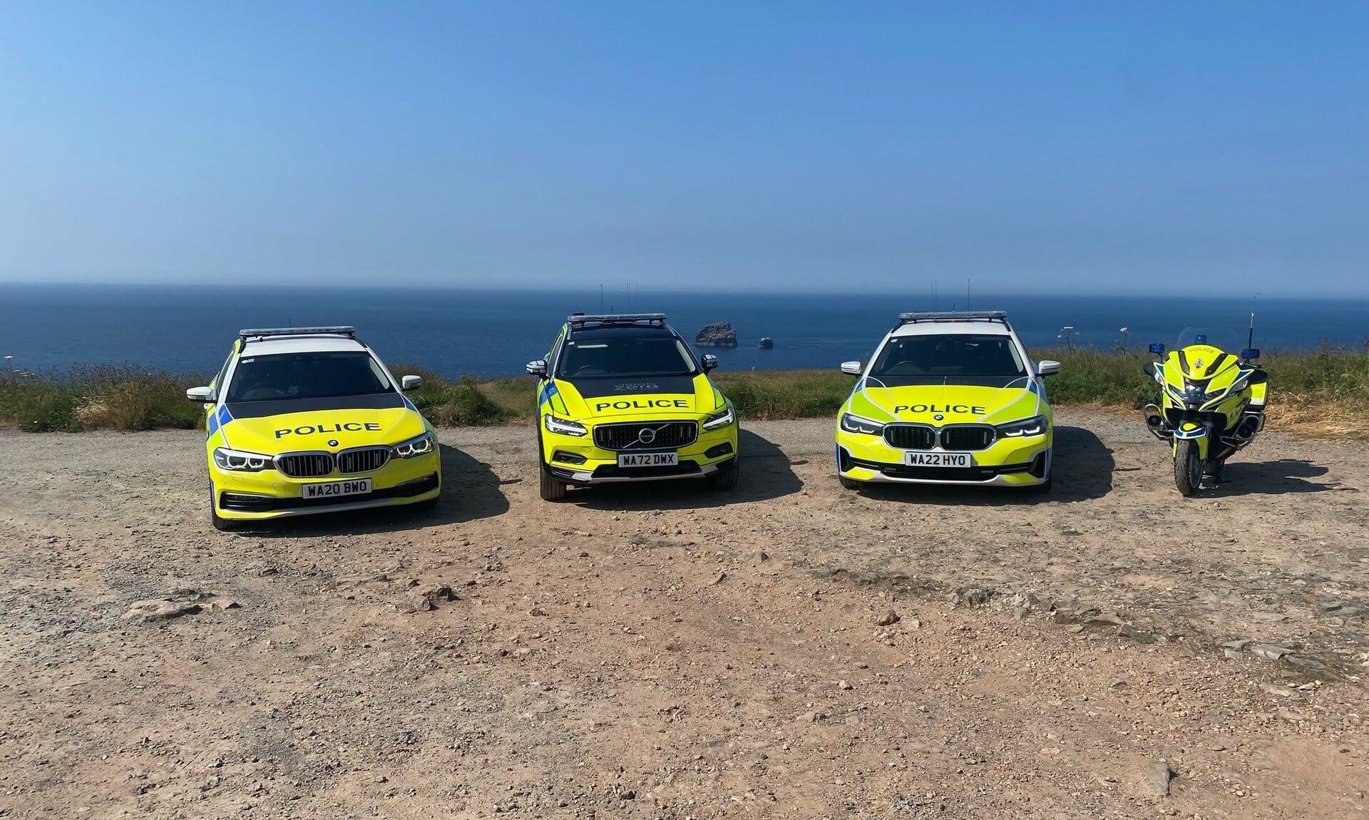 Three police cars and a police motorbike parked on a clifftop