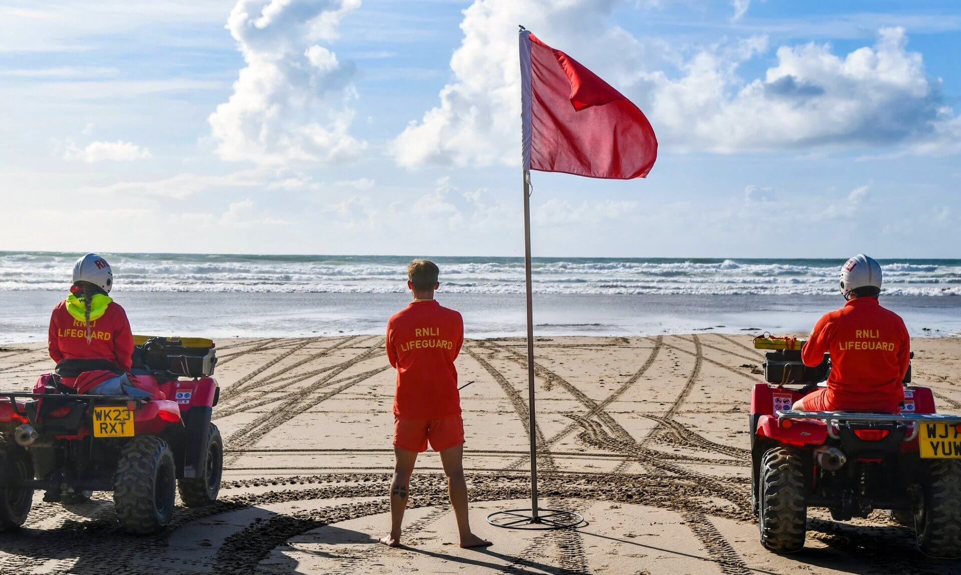 RNLI lifeguards on quad bikes watching the sea beside a red flag at Perran Sands