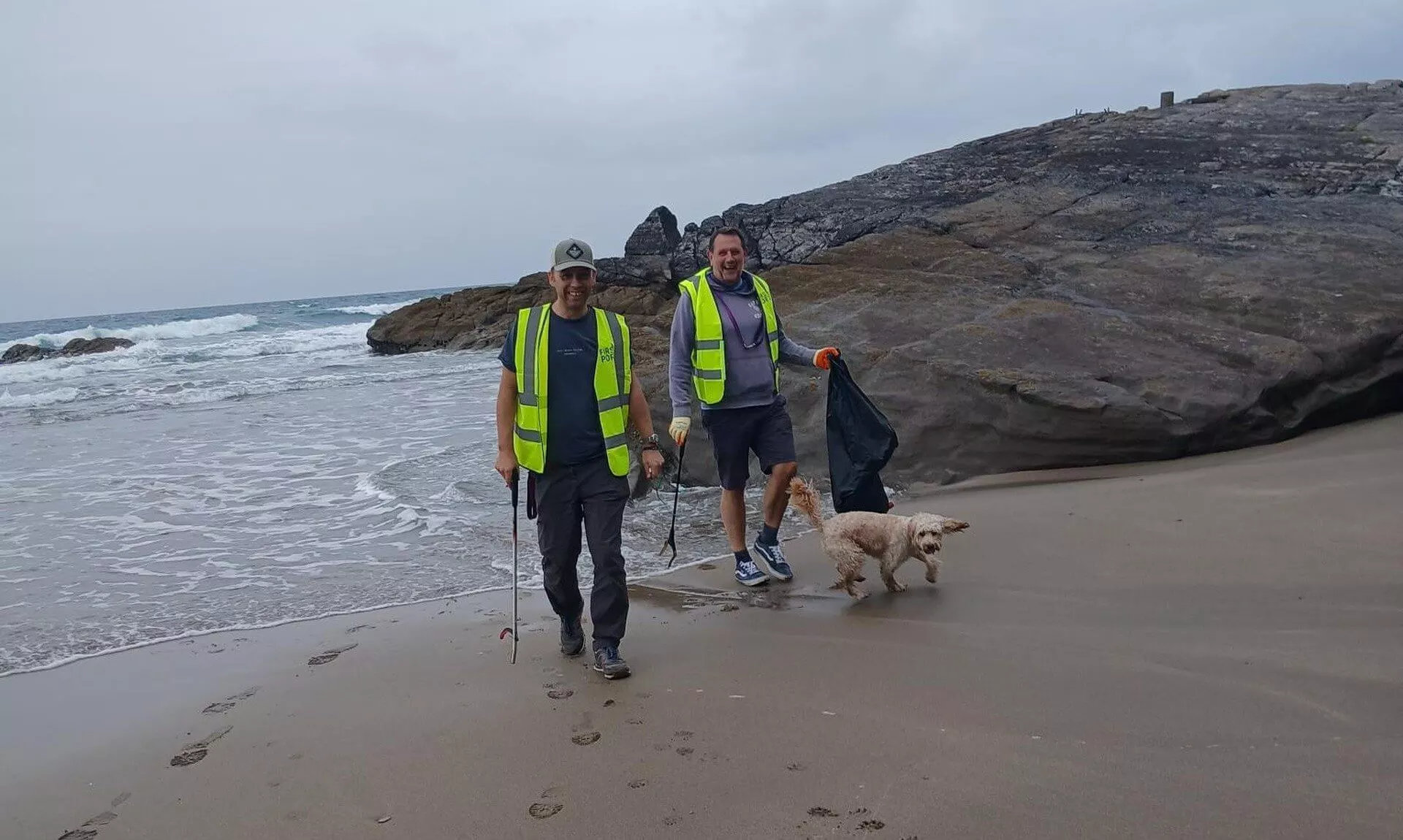 Two beach clean volunteers in hi-vis vests with a dog at Tregonhawke Beach