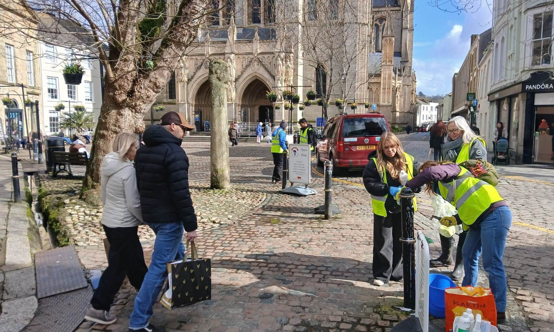 Volunteers in hi vis cleaning street furniture by Truro Cathedral