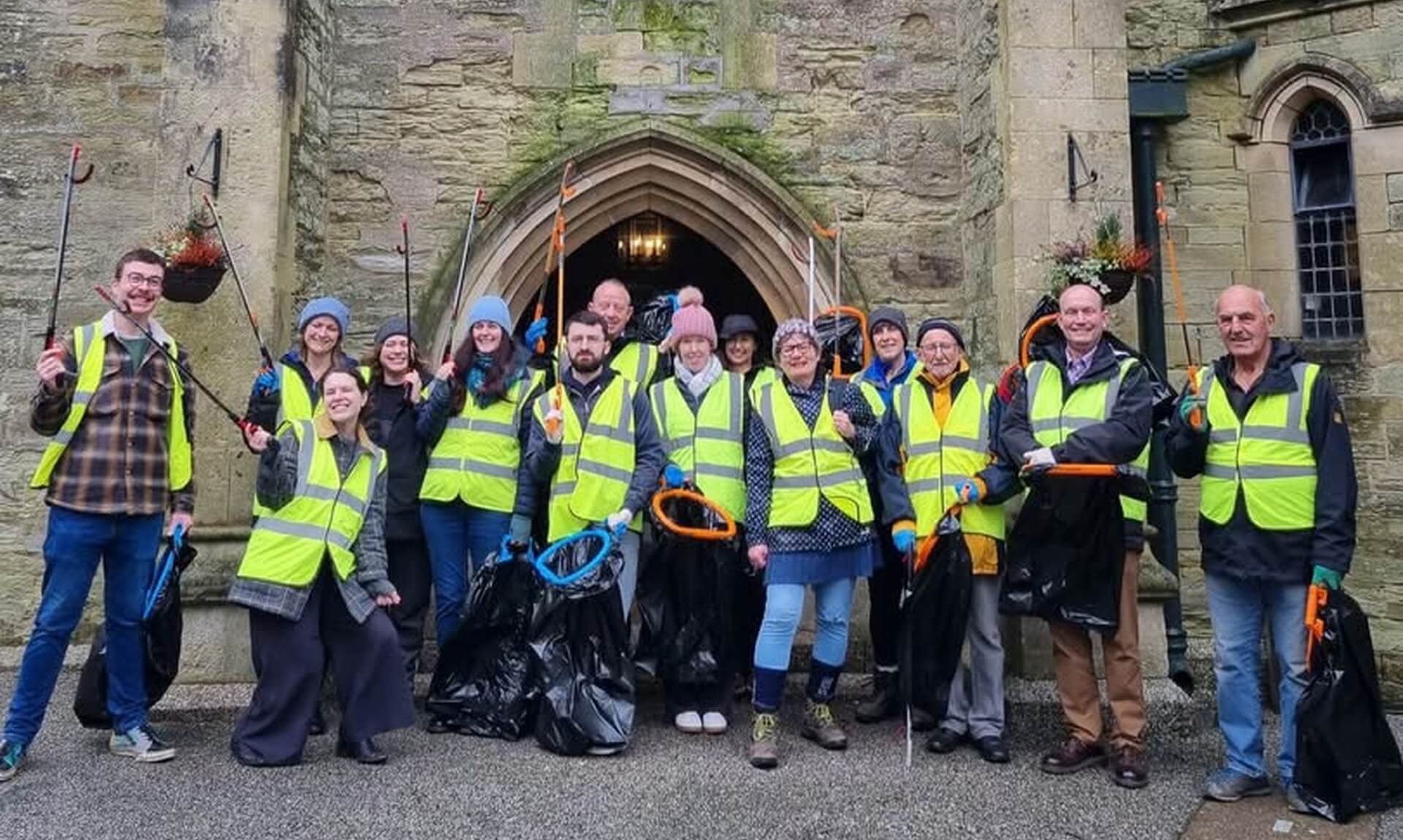 Volunteers in high-vis vests holding litter pickers and black bags outside a stone building in Truro