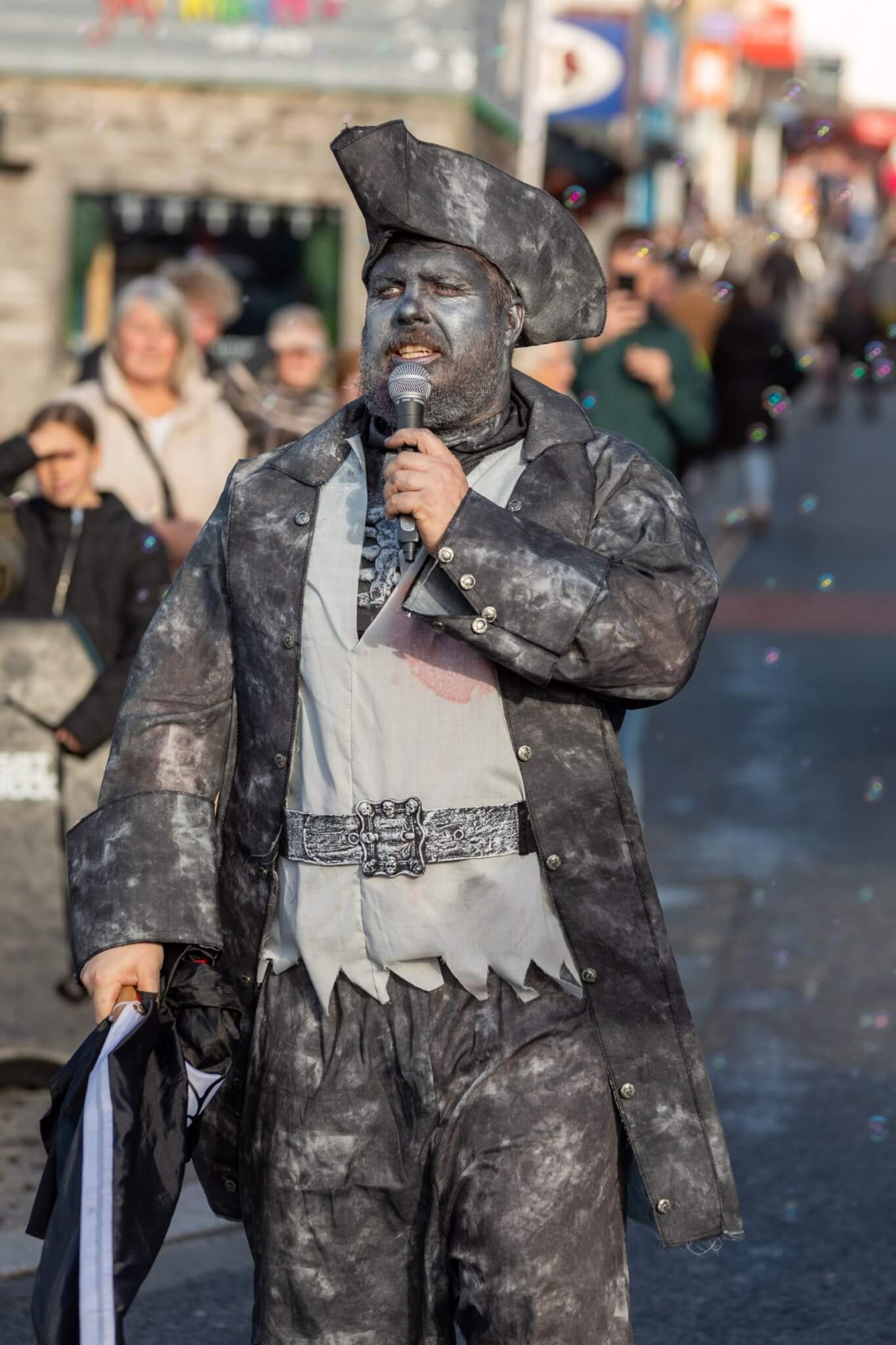 A performer in grey pirate costume speaking into a microphone at the Newquay Zombie Crawl