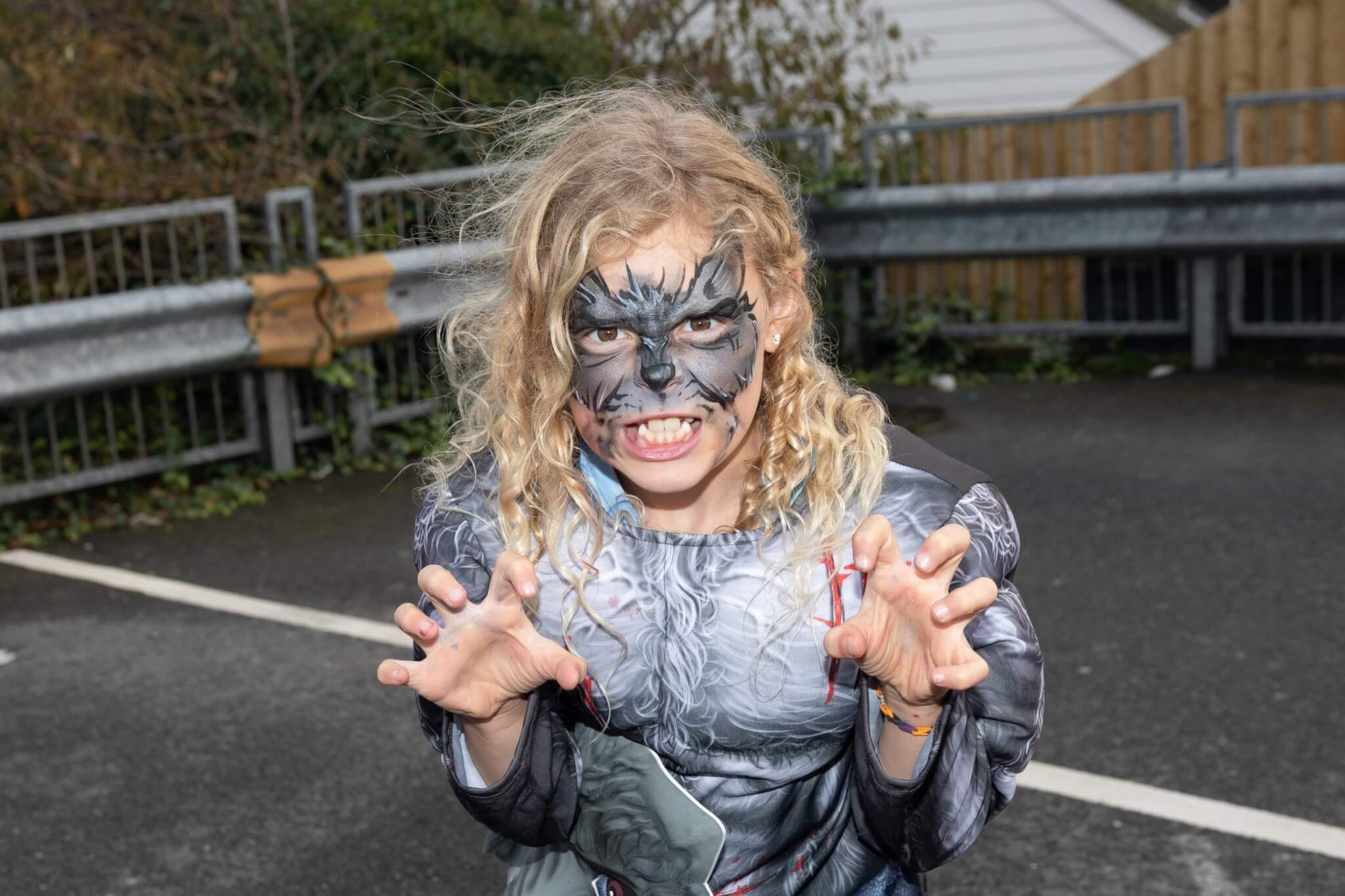 A child in werewolf face paint and costume posing with claws raised