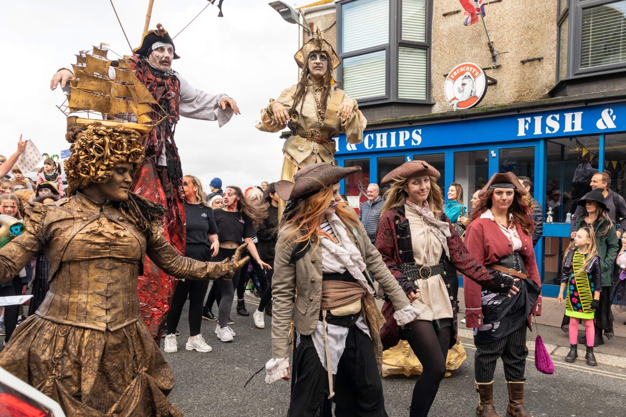 Stilt walkers and costumed pirates leading the Newquay Zombie Crawl past a fish and chip shop